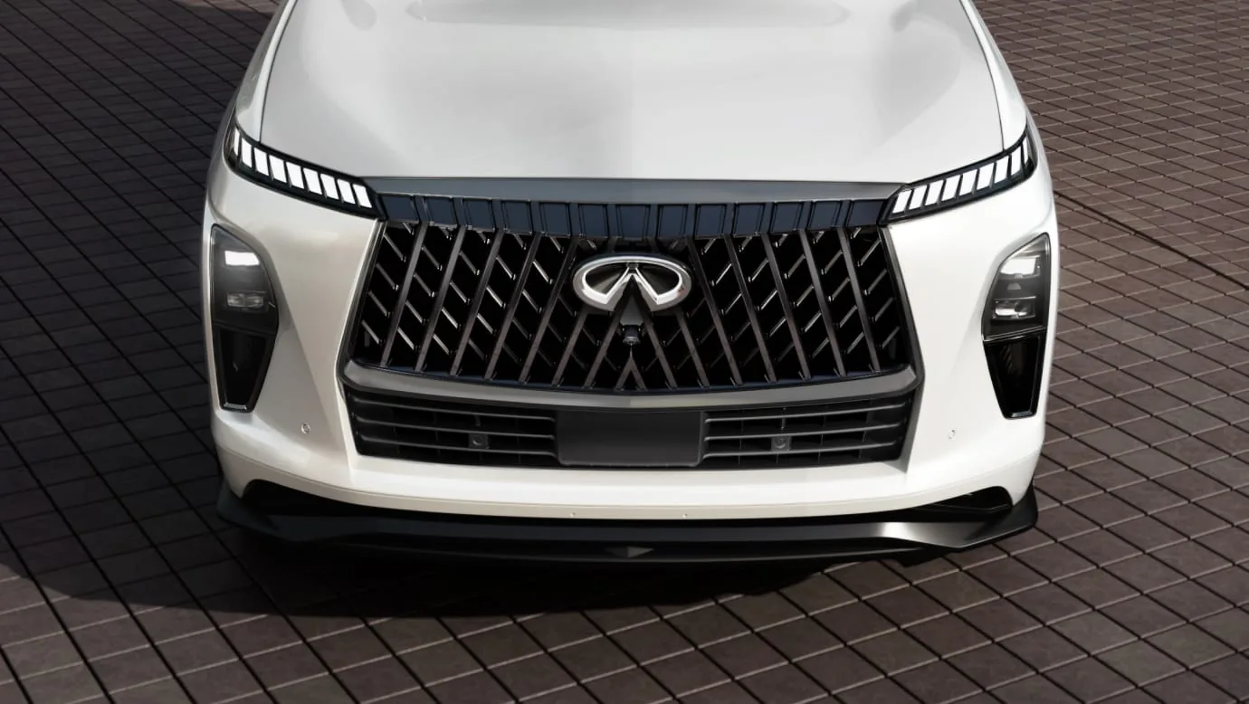 High-angle front close-up of a pearl white 2027 INFINITI QX80 SPORT showing the gloss-black double-arch grille, chrome emblem, and digital piano-key LED lights.