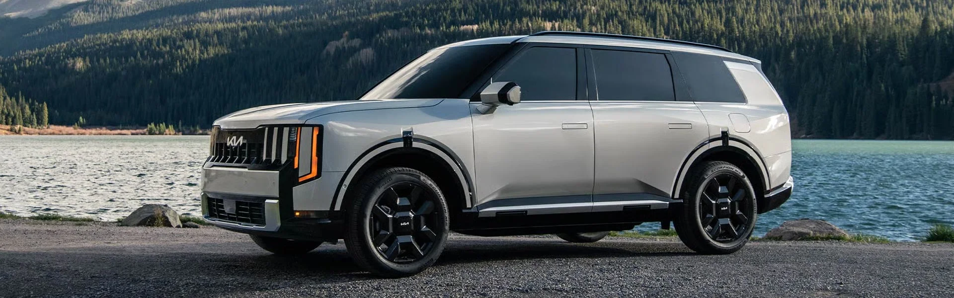 Silver 2027 Kia Telluride Hybrid driving on a lakeside mountain road