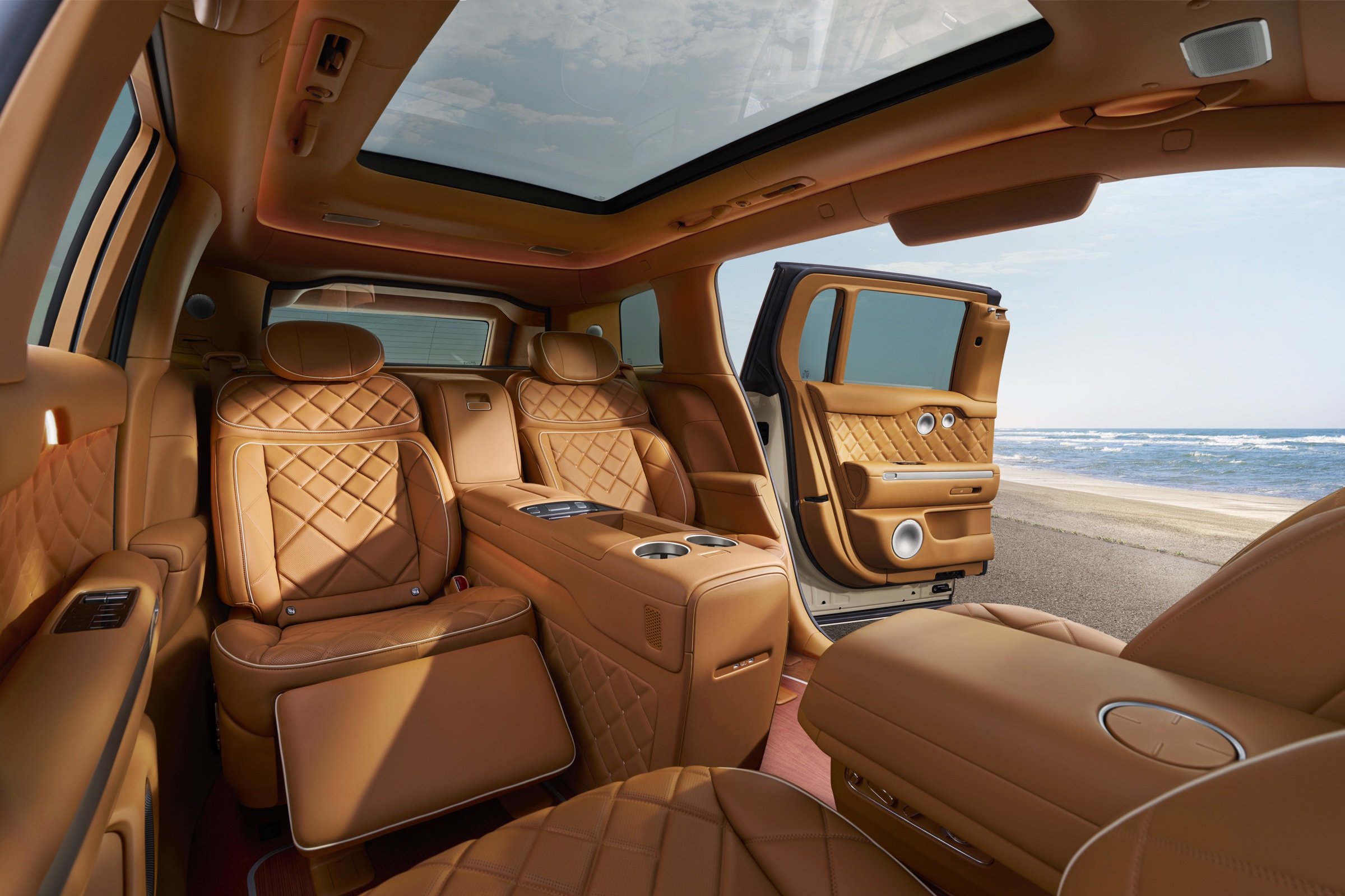 Quilted tan leather rear cabin of the GV90 with the door open to a coastal landscape