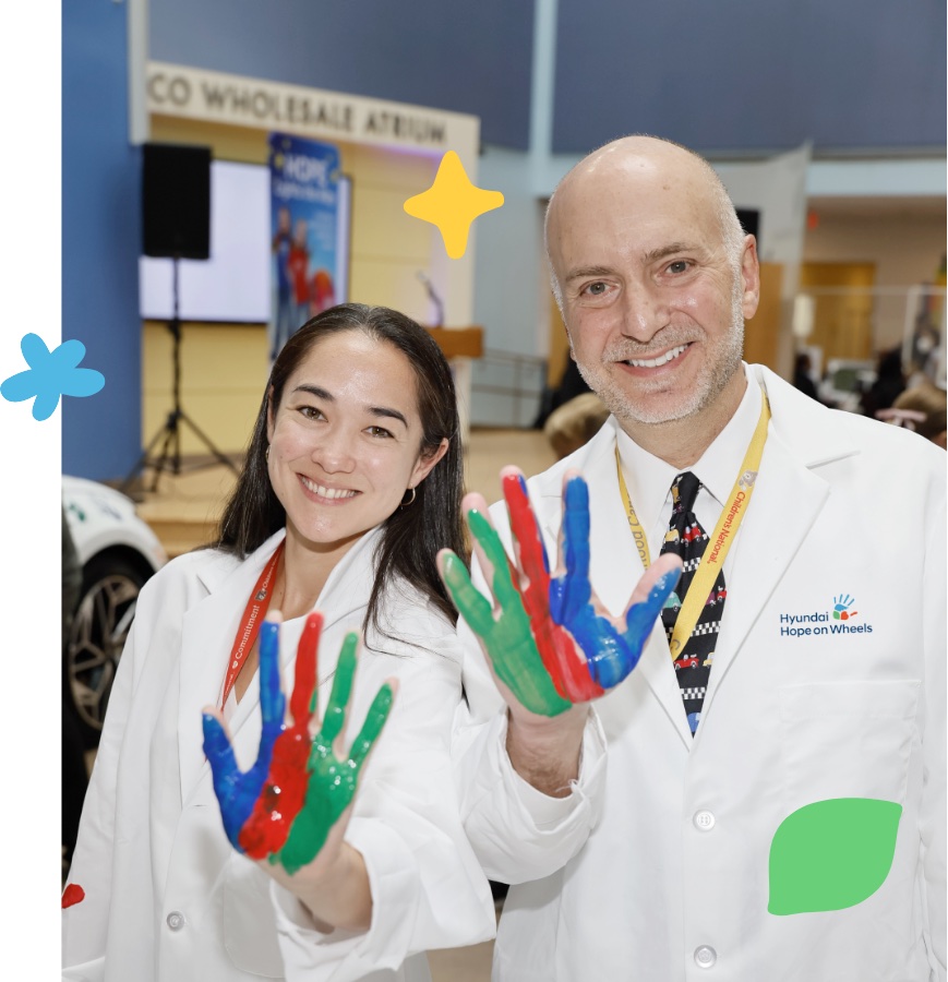 Doctors in Hyundai Hope on Wheels lab coats holding painted hands after a handprint ceremony