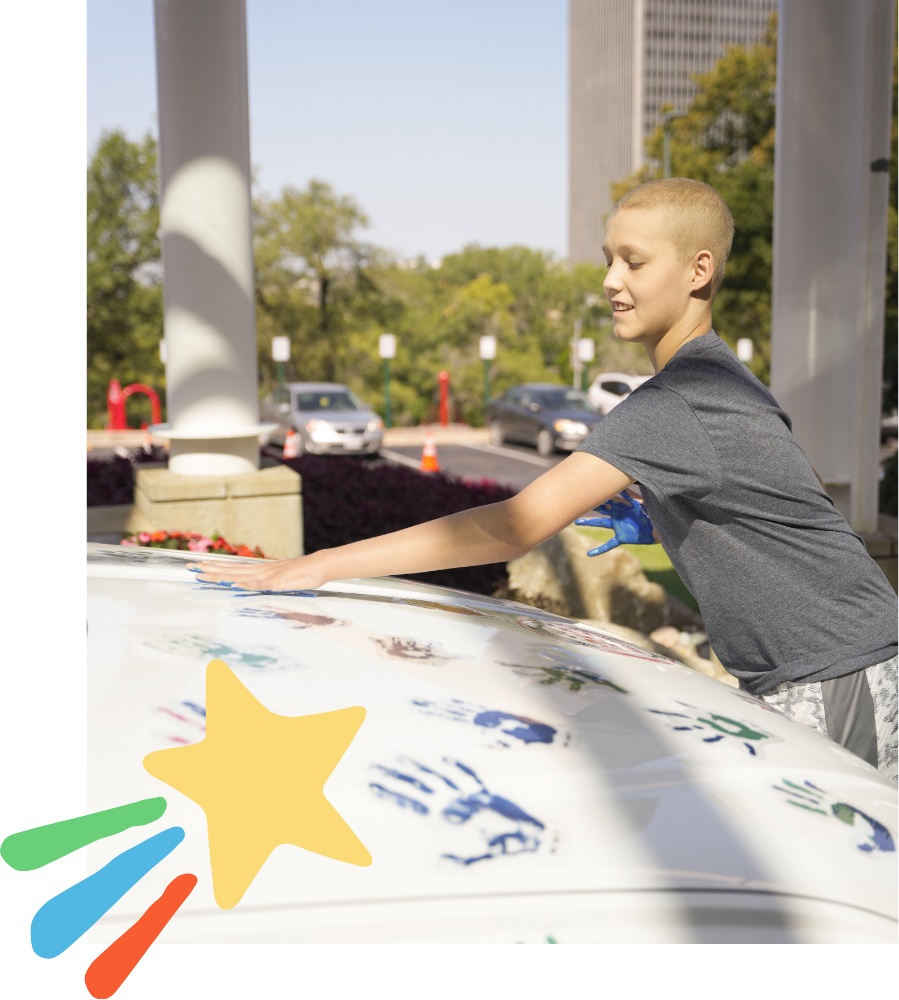 A child pressing a painted hand onto a white Hyundai covered in colorful handprints