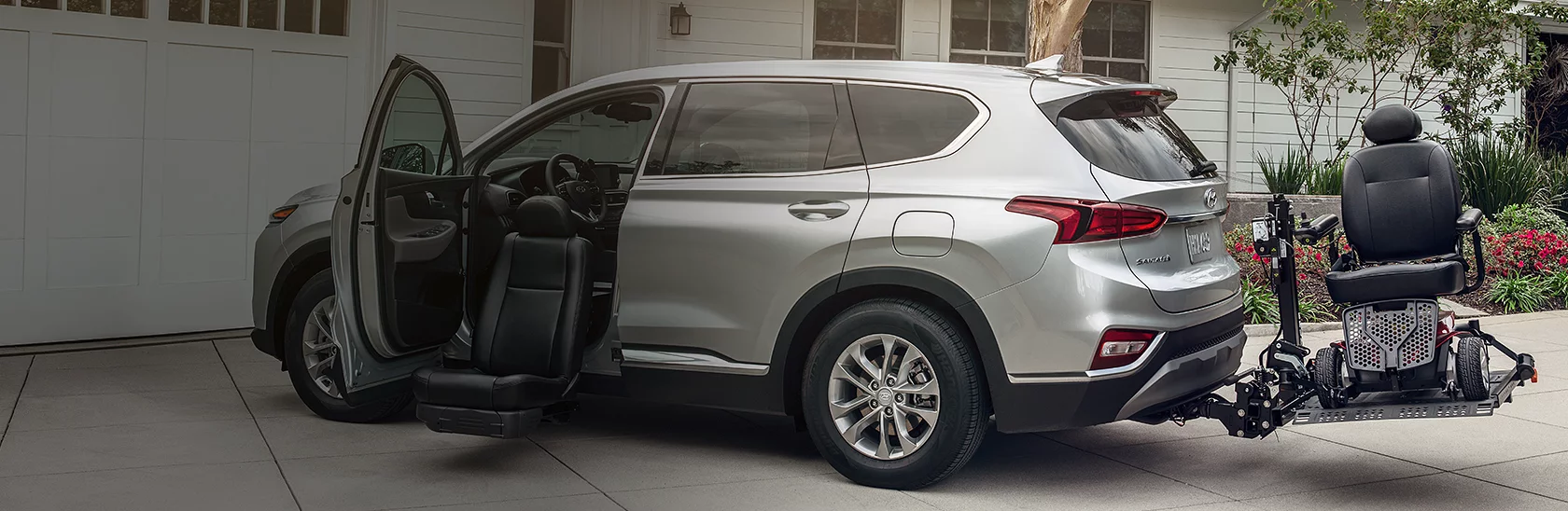 Silver Hyundai Santa Fe with a hitch-mounted wheelchair lift and a swivel passenger seat extended beside the open door