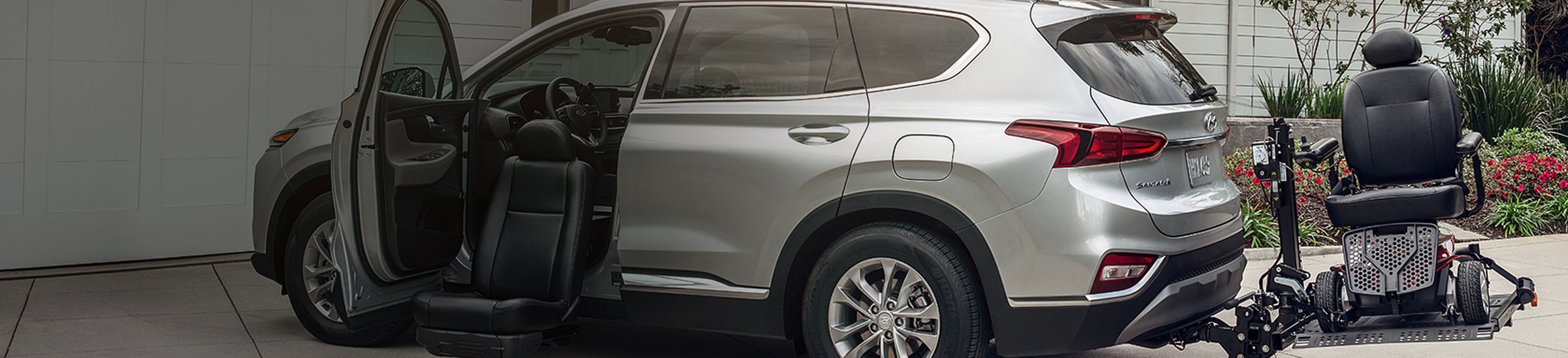 Silver Hyundai Santa Fe with a hitch-mounted wheelchair lift and a swivel passenger seat extended beside the open door