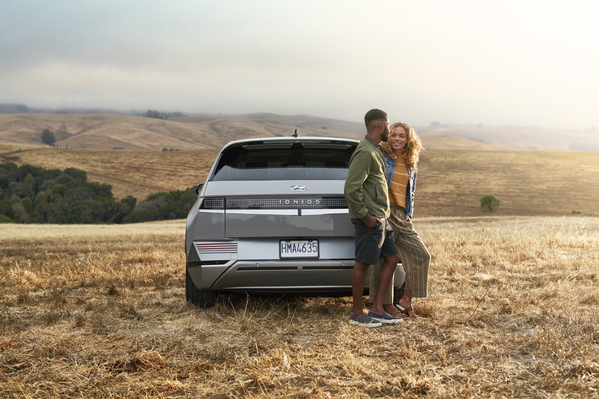 Couple standing beside a Hyundai IONIQ 5 in a grassy landscape
