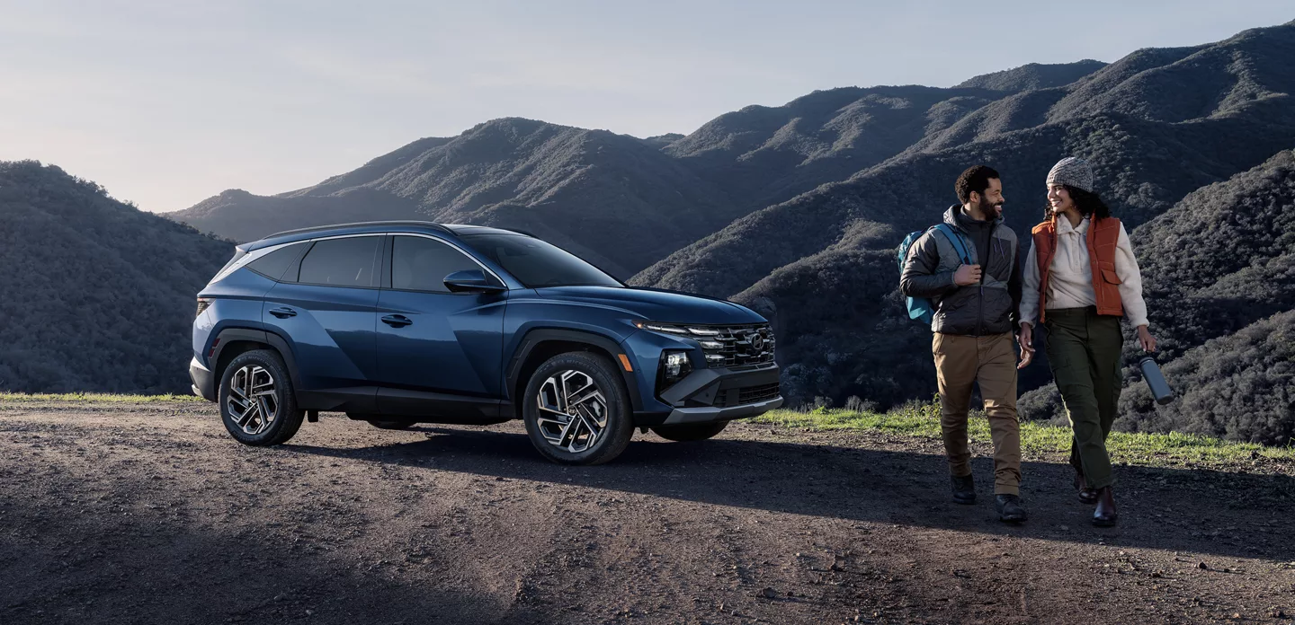Couple hiking beside a blue Hyundai Tucson in the mountains