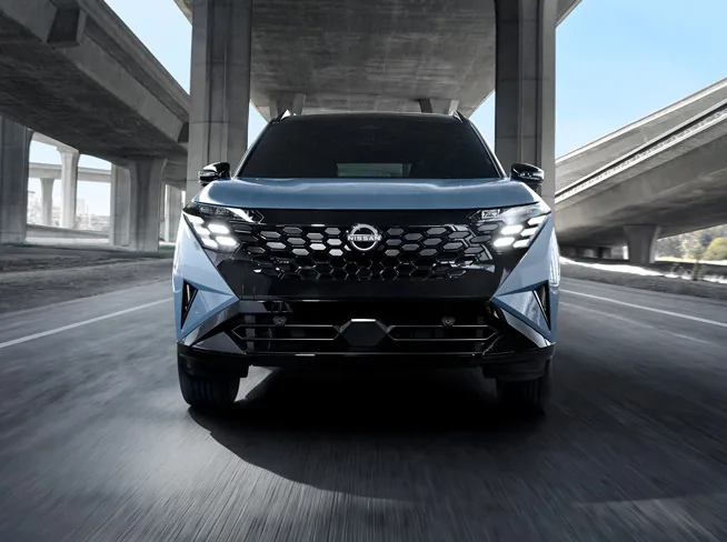 Front view of the 2027 Nissan Rogue Hybrid driving toward the camera on a highway under an overpass.