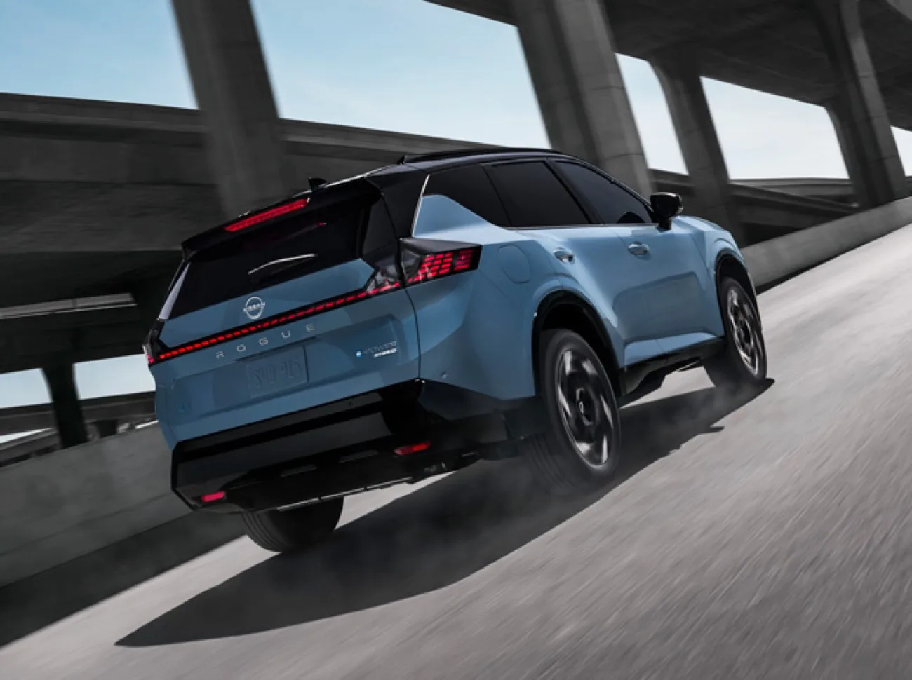 Front view of the 2027 Nissan Rogue Hybrid driving toward the camera on a highway under an overpass.