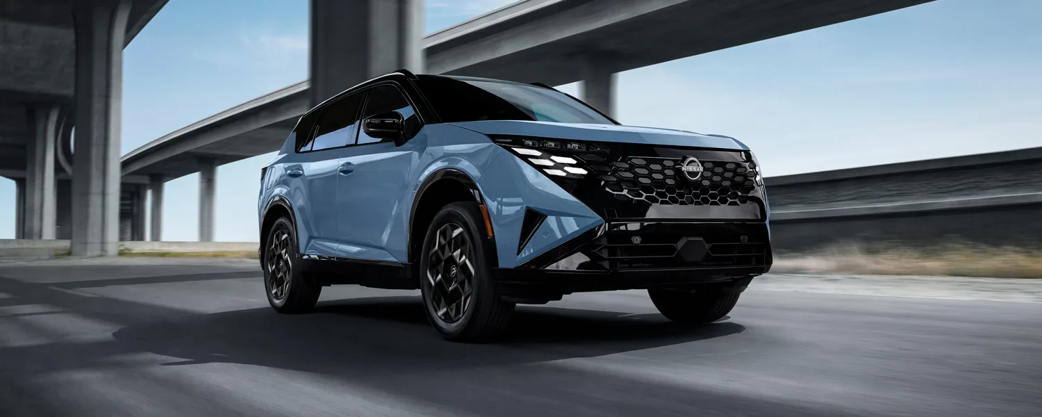 Front three-quarter view of the 2027 Nissan Rogue Hybrid driving on a highway under concrete overpasses.
