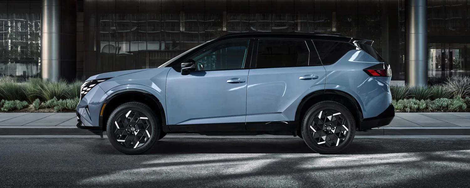 Side profile of the 2027 Nissan Rogue Hybrid parked at night in front of a modern building.