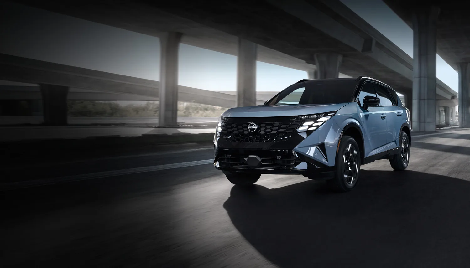 The all-new 2027 Nissan Rogue Hybrid in light blue, viewed from a high three-quarter front angle in a spotlight under a concrete overpass.