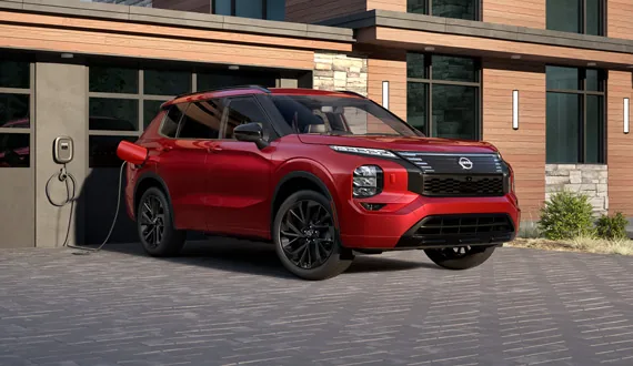 2026 Nissan Rogue Plug-In Hybrid in red, plugged in beside a home charger.