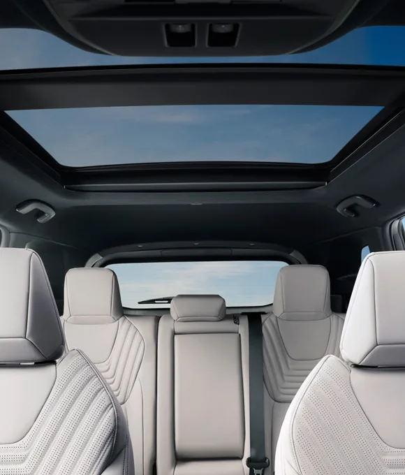 Rear cabin of the 2027 Nissan Rogue Hybrid with quilted light seating and a panoramic moonroof under blue sky.