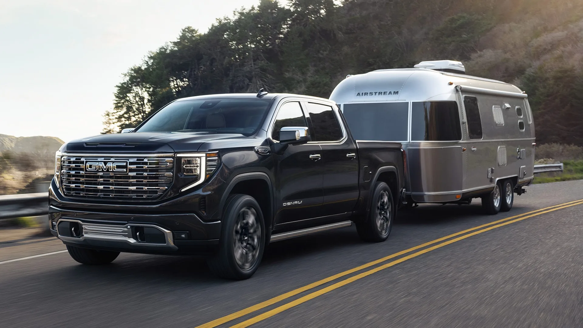 GMC Sierra 1500 pickup towing a silver Airstream travel trailer on an open road