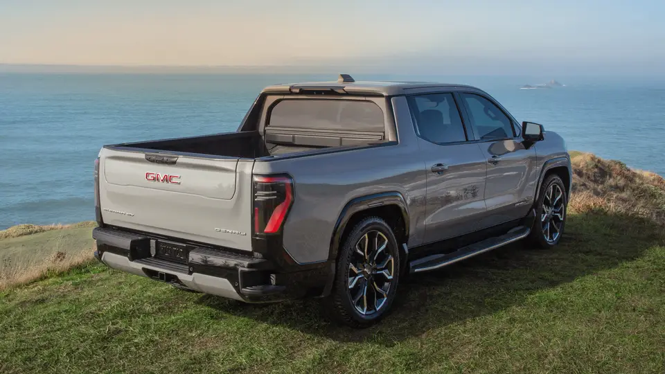 Rear view of a GMC Sierra EV pickup parked on a hill overlooking water with the MultiPro Tailgate folded down