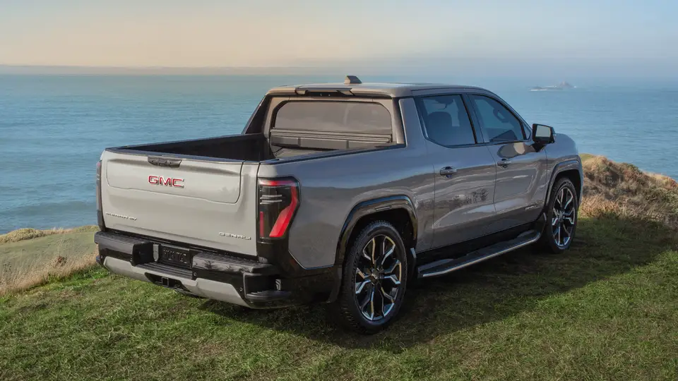 Rear view of a GMC Sierra EV pickup parked on a hill overlooking water with the MultiPro Tailgate folded down